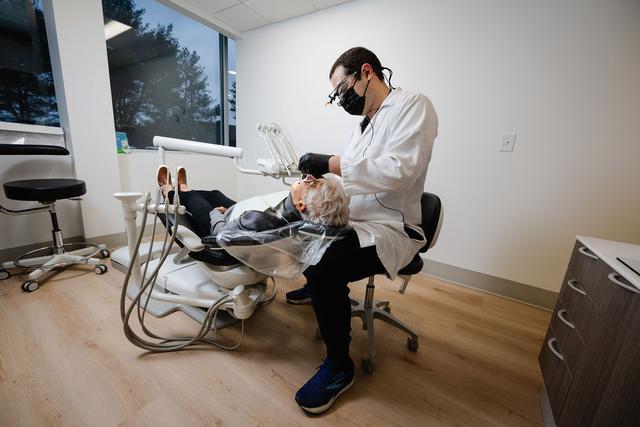 A dentist wearing a mask and loupes works on a patient lying in a dental chair.
