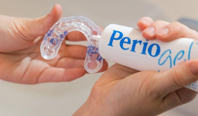 a person is holding a tooth whitening device and a tube of perio gel .