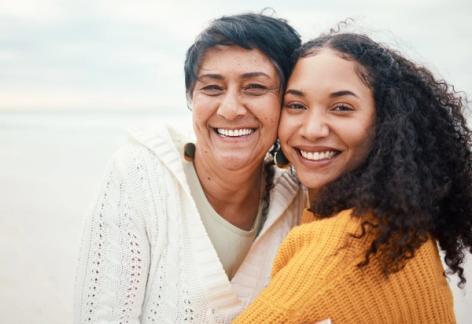 an older woman and a younger woman are posing for a picture on the beach .