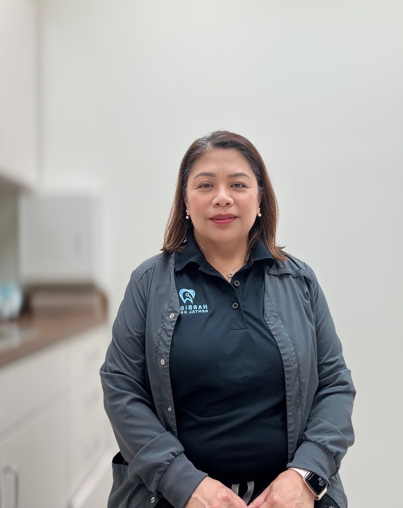 a woman wearing a black shirt and a grey jacket is standing in front of a white wall .