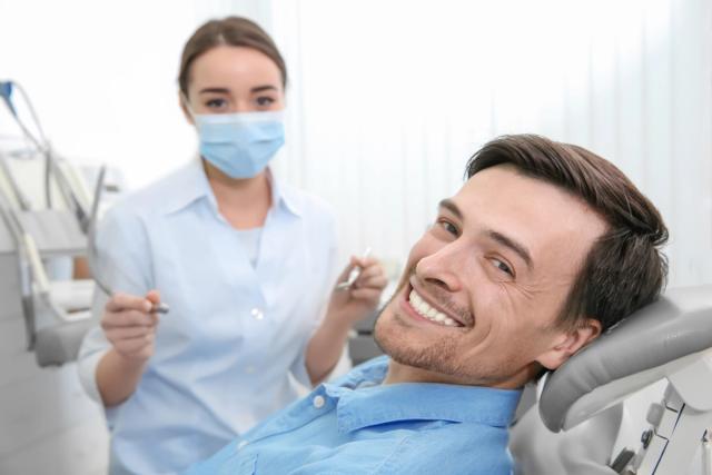 a man is smiling while sitting in a dental chair next to a female dentist .