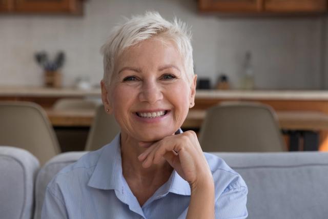 an older woman is smiling while sitting on a couch with her hand on her chin .