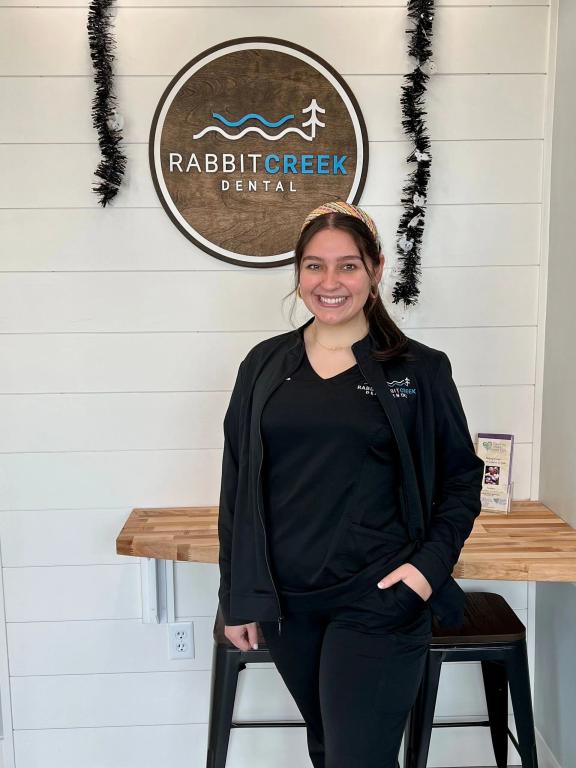 a woman is standing in front of a rabbit creek dental sign .