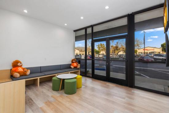 a waiting room with a couch , table , ottomans and two teddy bears .
