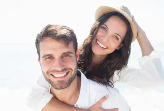a man is giving a woman a piggyback ride and they are smiling for the camera .