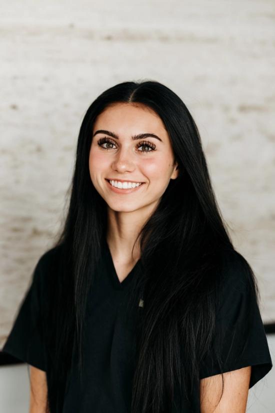 Headshot of a smiling young woman with long dark hair in a black scrub top.