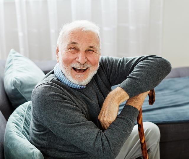 an elderly man is sitting on a couch with a cane and smiling .