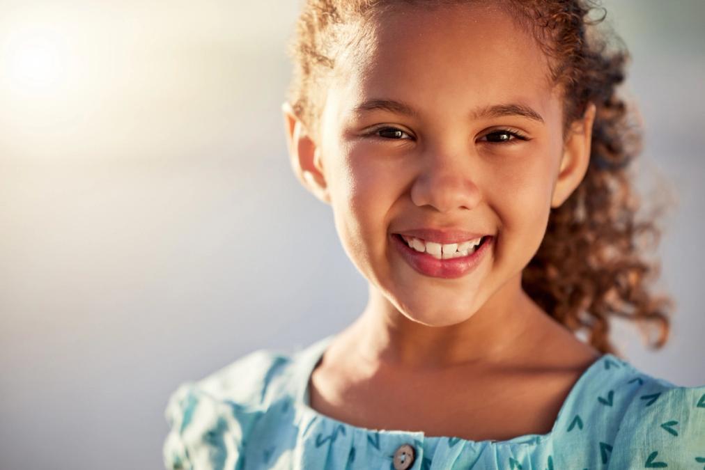 A young girl with curly hair smiles at the camera.