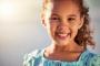 A young girl with curly hair smiles at the camera.