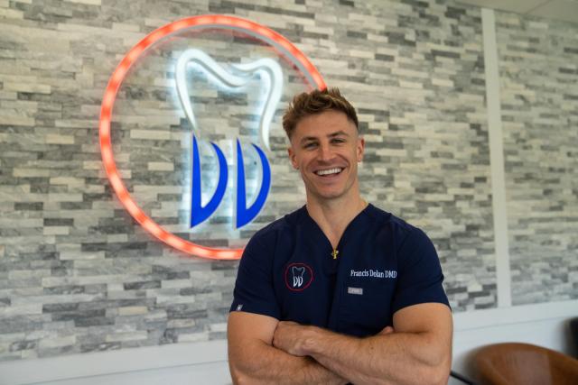 a dentist is standing in front of a dental office with his arms crossed .