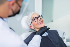 Dentist examining a smiling older woman in a dental chair.