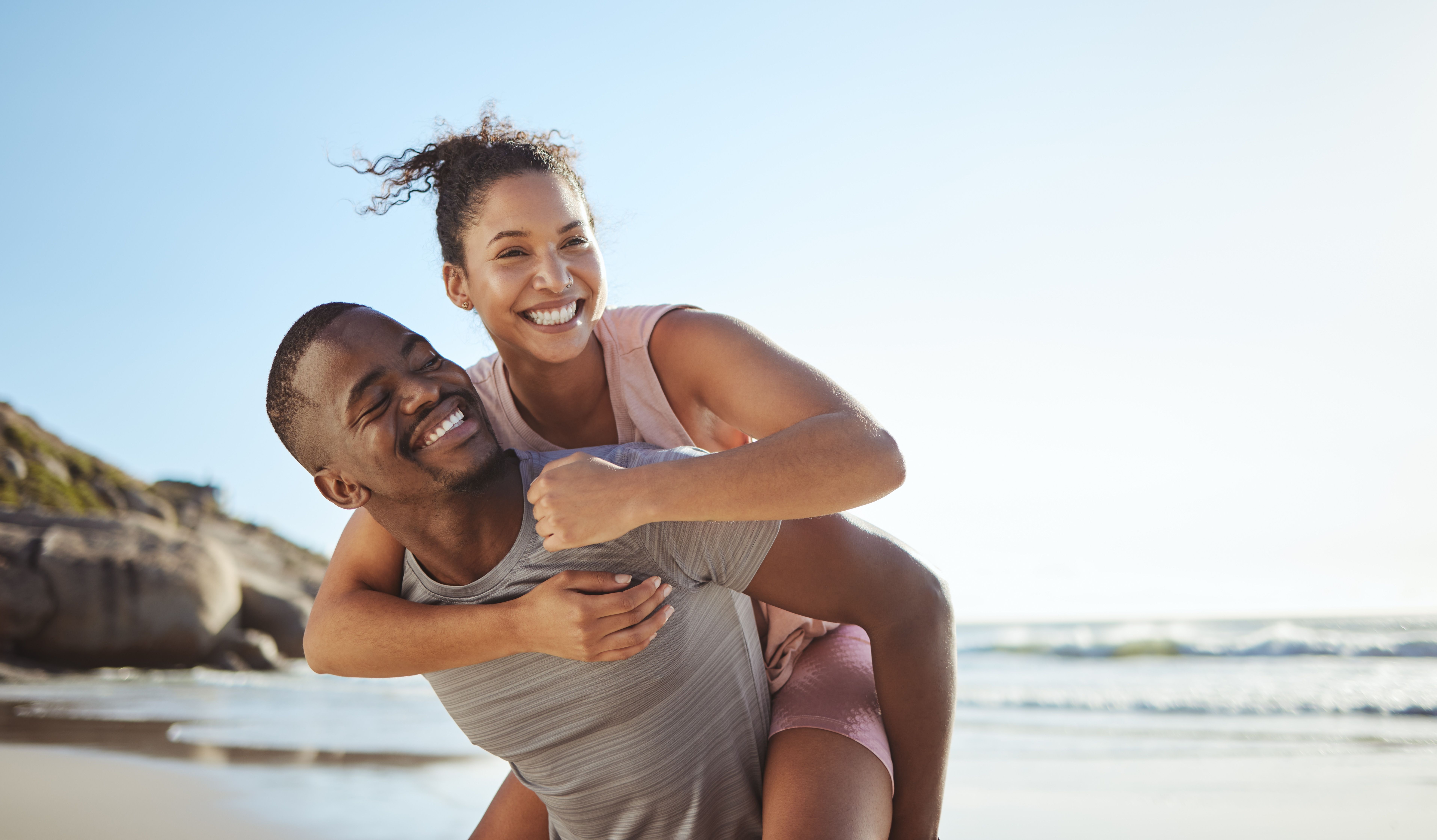 a man is carrying a woman on his back on the beach .