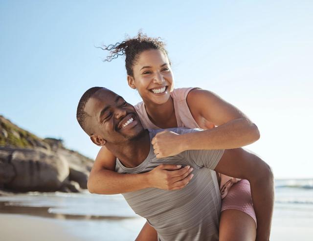a man is carrying a woman on his back on the beach .
