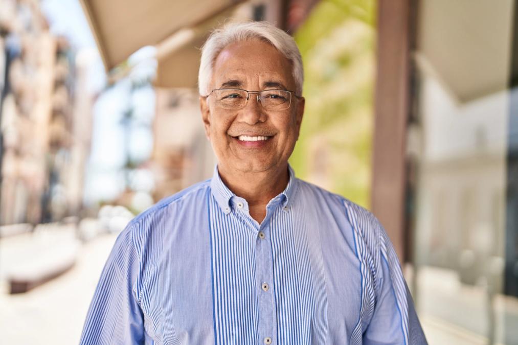an older man wearing glasses and a blue shirt is smiling for the camera .