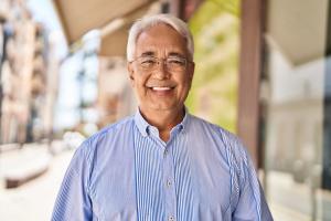 Smiling older man with white hair and glasses wearing a blue striped shirt outdoors.