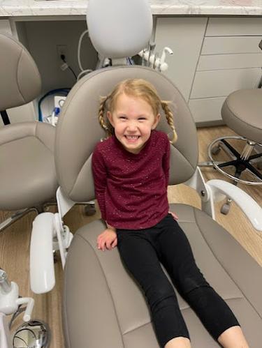 a little girl wearing a tie dye apron is sitting in a dental chair