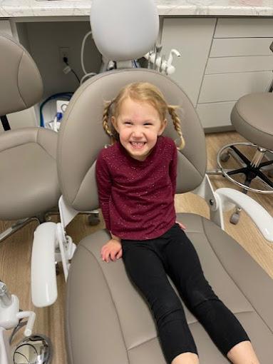 a little girl is sitting in a dental chair and smiling .