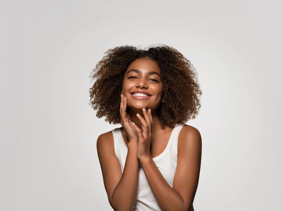 a woman with curly hair is smiling and touching her face .