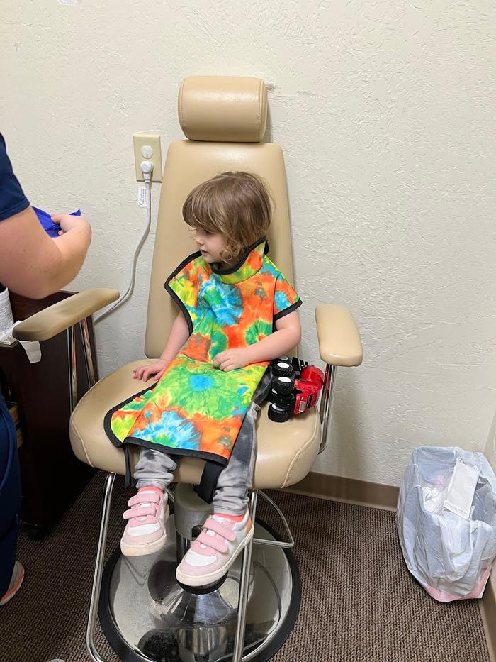 a little girl wearing a tie dye apron is sitting in a dental chair