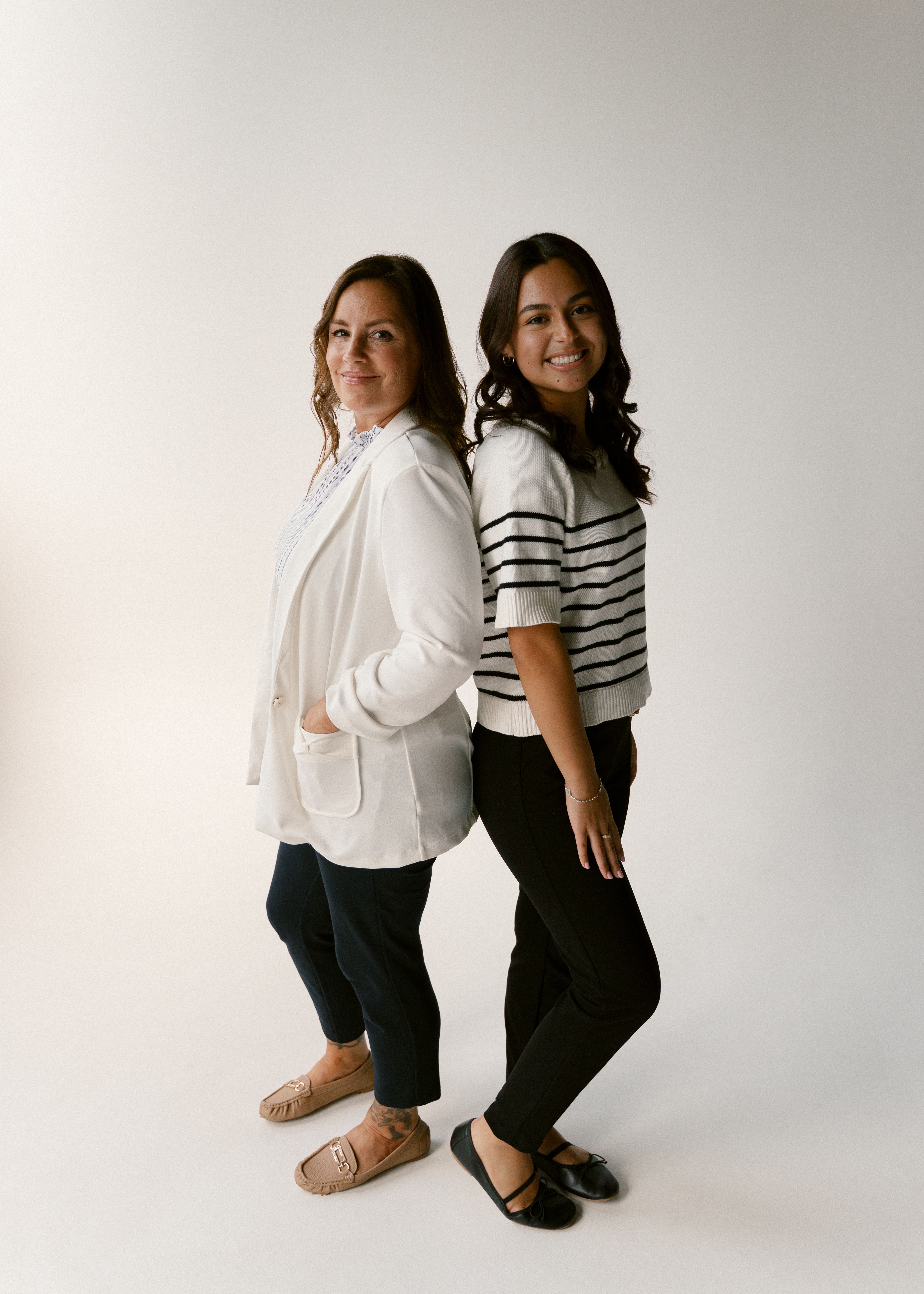 two women standing back to back with their hands in their pockets