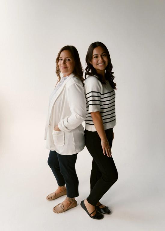 two women standing back to back with their hands in their pockets