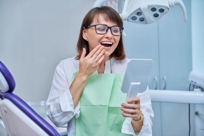 a woman is sitting in a dental chair looking at her teeth in a mirror .