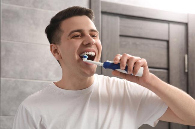 a young man is brushing his teeth with an electric toothbrush in the bathroom .