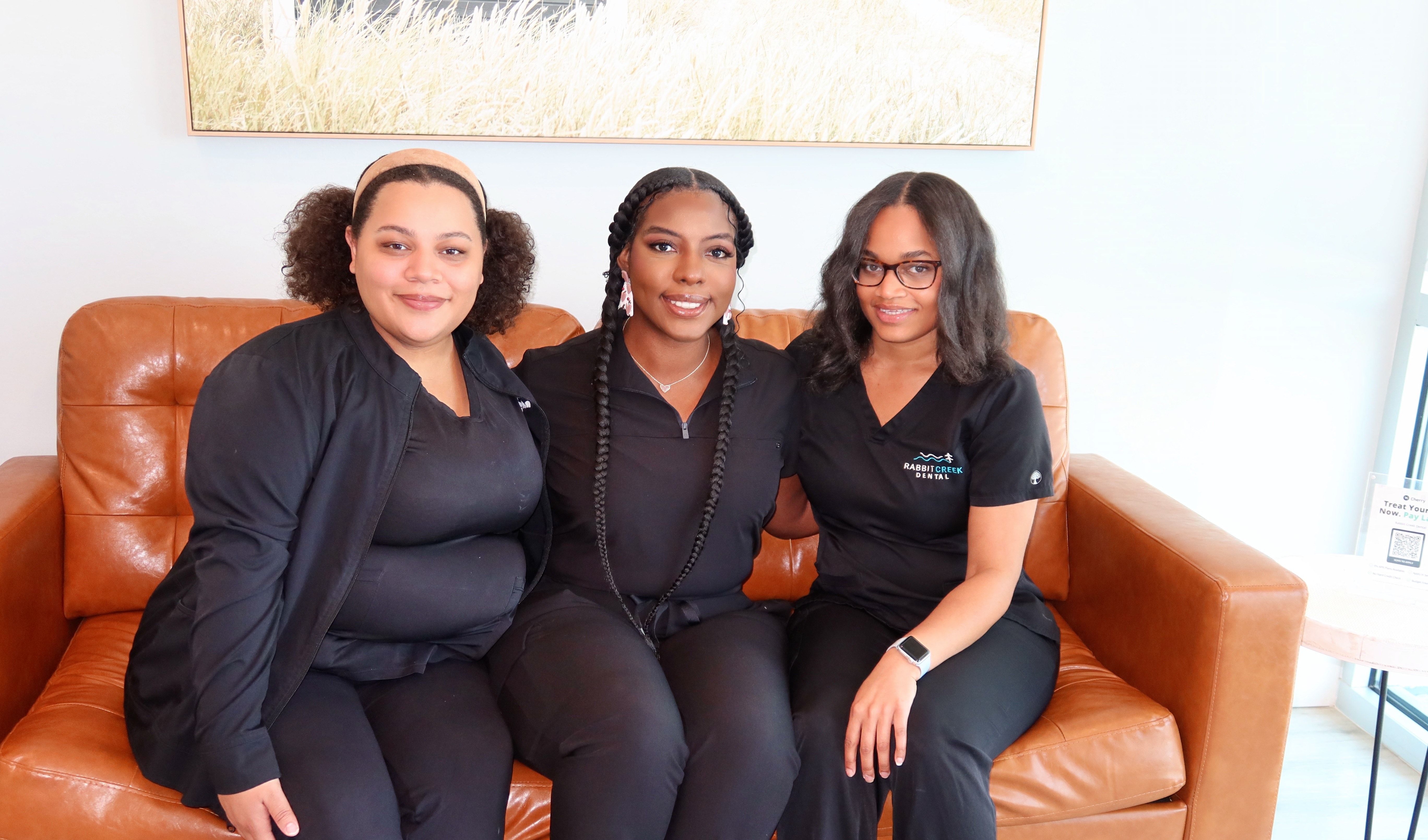 three women in scrubs are sitting on a couch and posing for a picture .