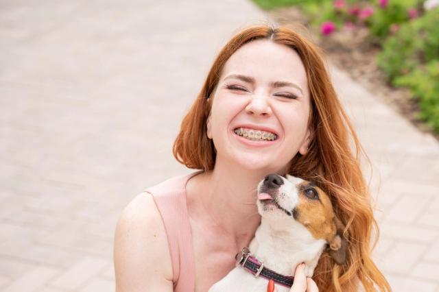 a woman with braces is holding a small dog in her arms .
