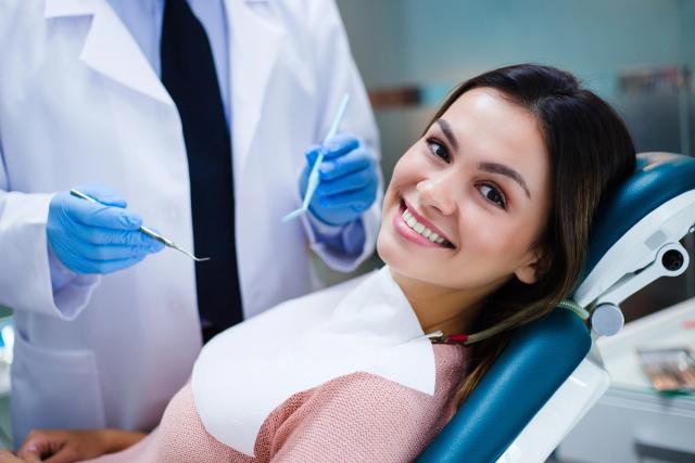 a woman is sitting in a dental chair while a dentist examines her teeth .