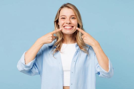a woman is pointing at her teeth and smiling .