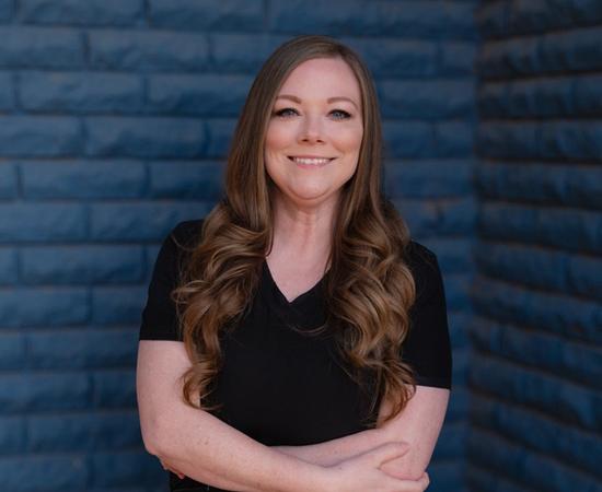 a woman in a black scrub top stands with her arms crossed in front of a blue brick wall