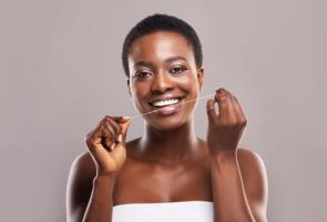 A smiling woman flossing her teeth.