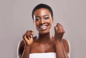 A smiling woman flossing her teeth.