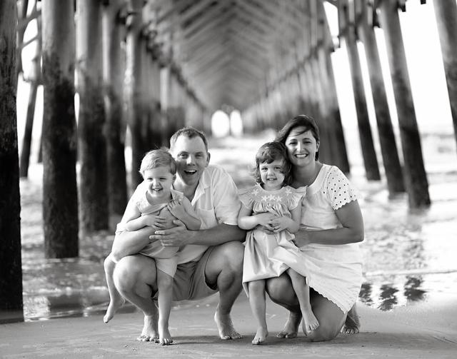 a black and white photo of a family posing for a picture under a pier .