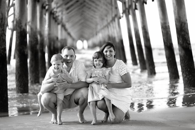 a black and white photo of a family posing for a picture under a pier .