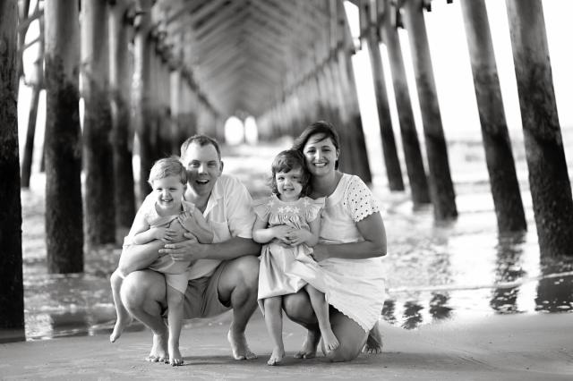 a black and white photo of a family posing for a picture under a pier .