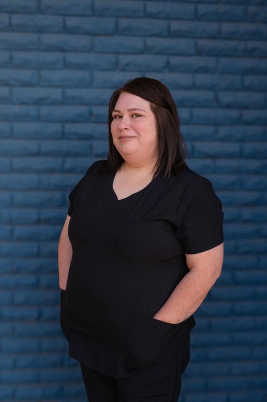 a woman wearing a black scrub top stands in front of a blue brick wall