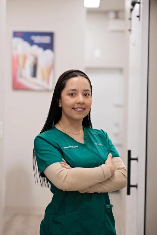 a woman in a green scrub is standing in a hallway with her arms crossed .