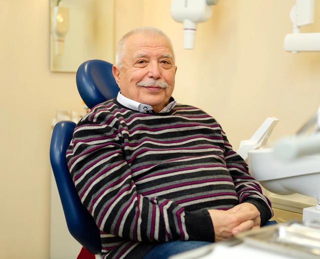 an elderly man is sitting in a dental chair and smiling .