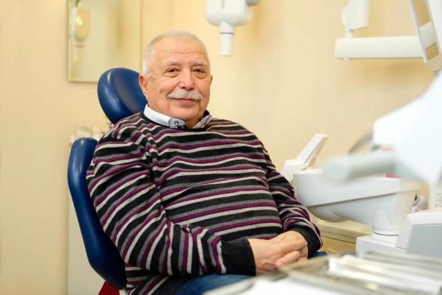 an elderly man is sitting in a dental chair and smiling .