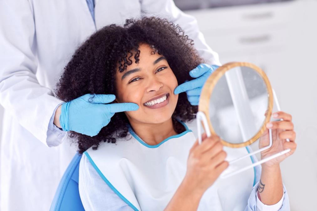 a woman is sitting in a dental chair looking at her teeth in a mirror .
