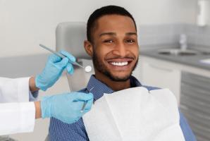 A smiling man in a dental chair with a dentist's gloved hands holding tools.