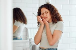 a woman is brushing her teeth in a bathroom and has a toothache .