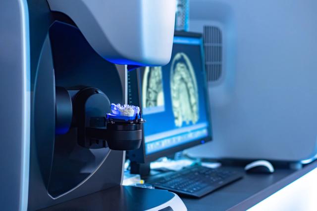 A dental 3D scanner digitizing a dental model, with digital teeth scans displayed on a monitor.