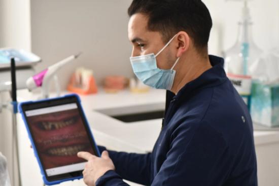 a dentist wearing a mask is using a tablet computer in a dental office .
