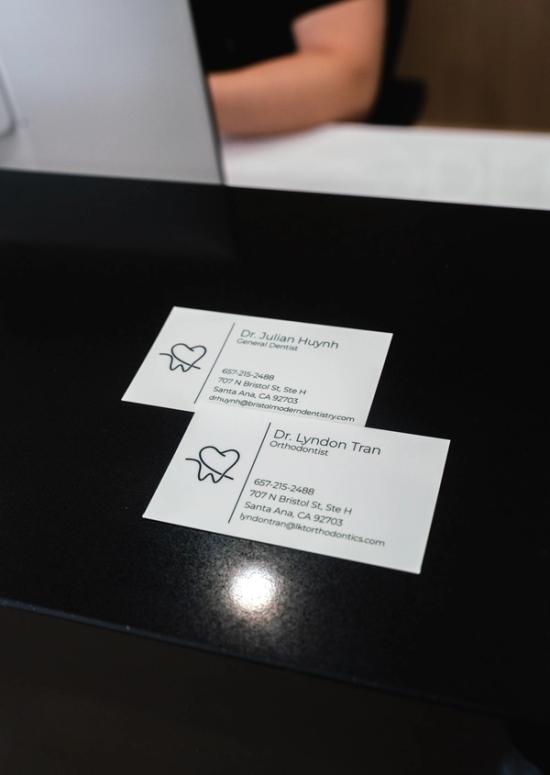 Two white business cards for Dr. Julian Huynh (General Dentist) and Dr. Lyndon Tran (Orthodontist) on a black table.