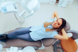 a woman is laying in a dental chair with her hands behind her head .