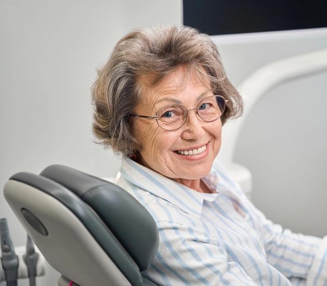 an elderly woman is smiling while sitting in a dental chair .
