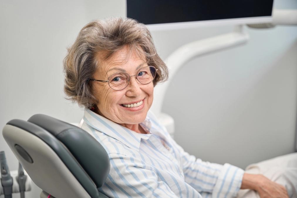 an elderly woman is smiling while sitting in a dental chair .